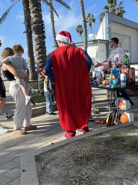 The Plumber Man in red cape handing out toys at community giveaway