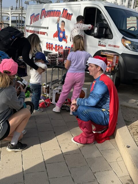 The Plumber Man kneeling to talk with child while giving gifts